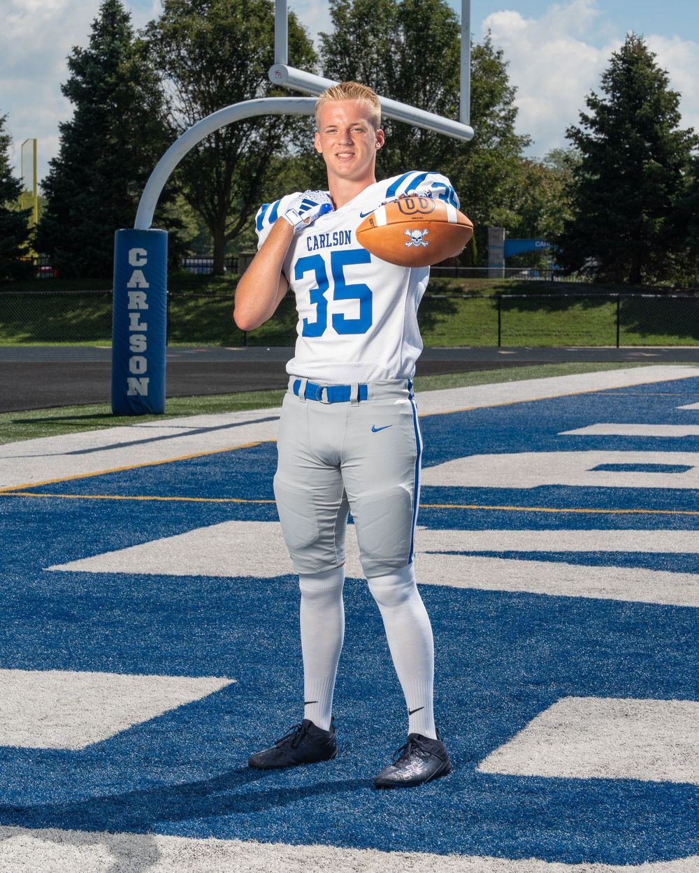 Carlson #35 football player in white and blue uniform holding a ball on a blue field turf.