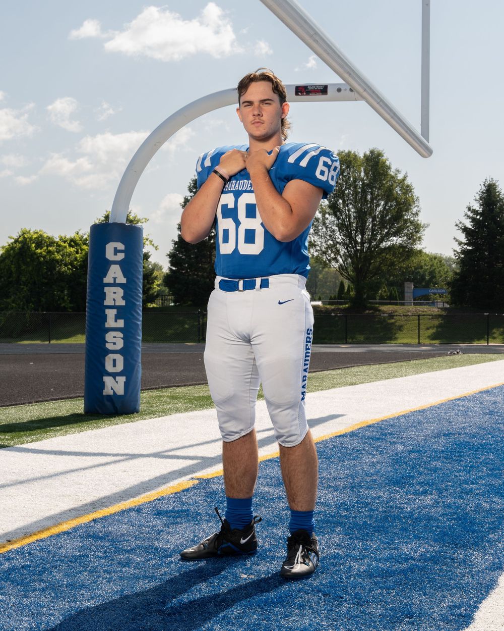 High school football player #68 in blue Carlson uniform poses on blue turf field near goal post.