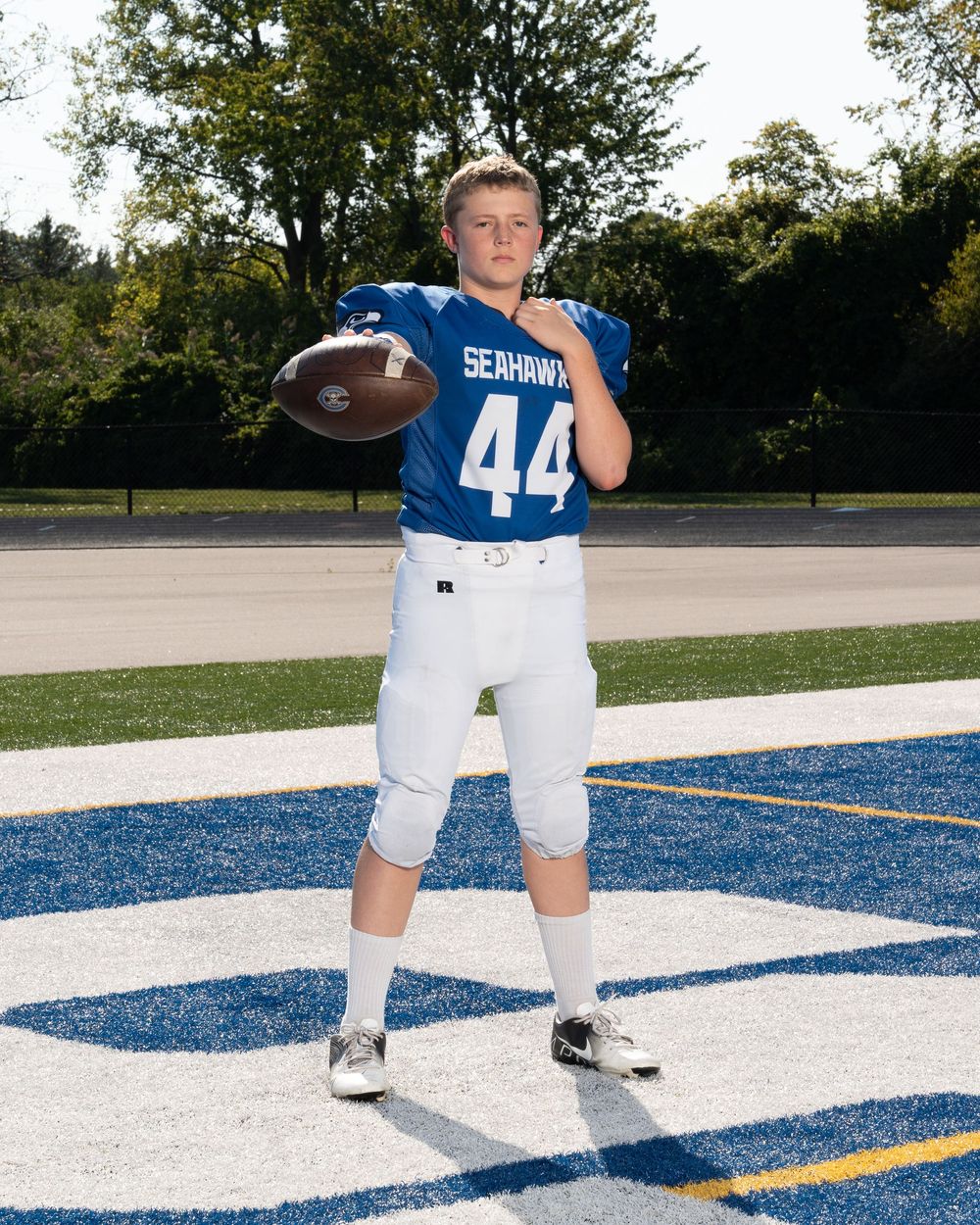 Youth football player #44 in blue Seahawks uniform poses with football on field.
