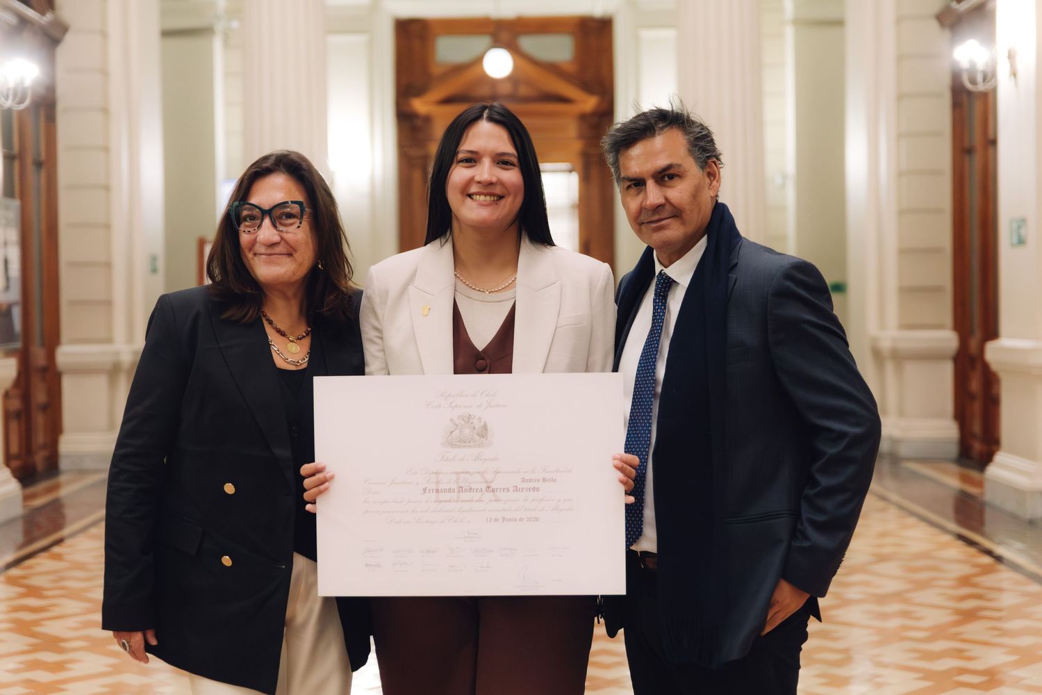 Three people pose proudly in an elegant hallway holding a formal certificate or diploma.