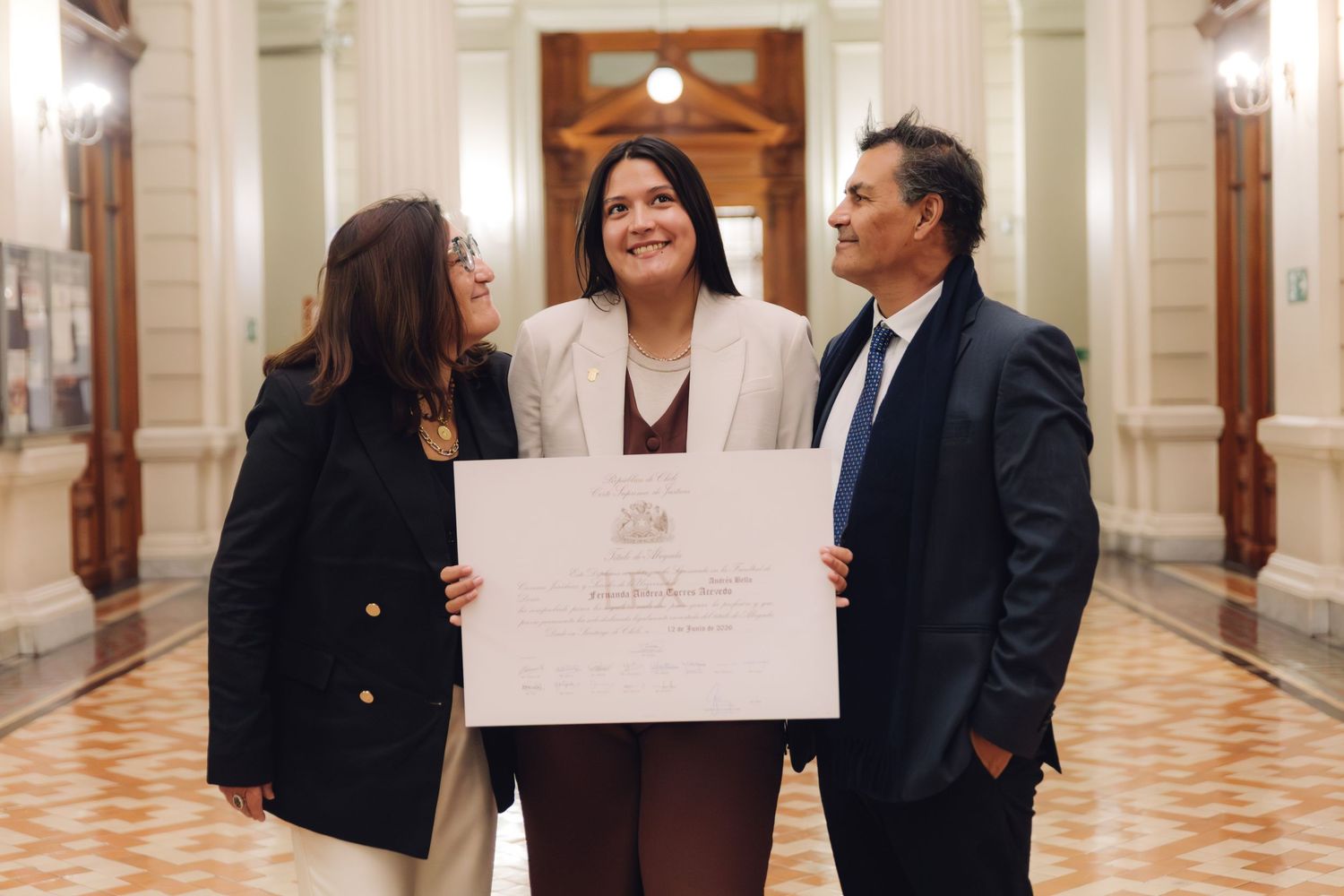 Three people share a joyful moment in a classical hallway, one holding a large official document.