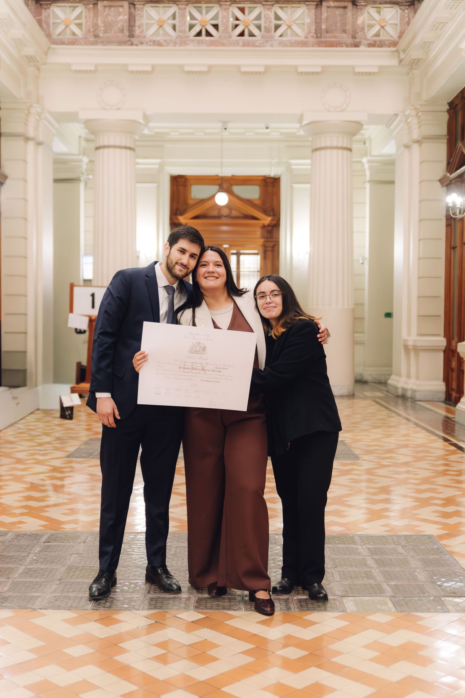 Three people pose proudly in elegant hall holding a diploma certificate.