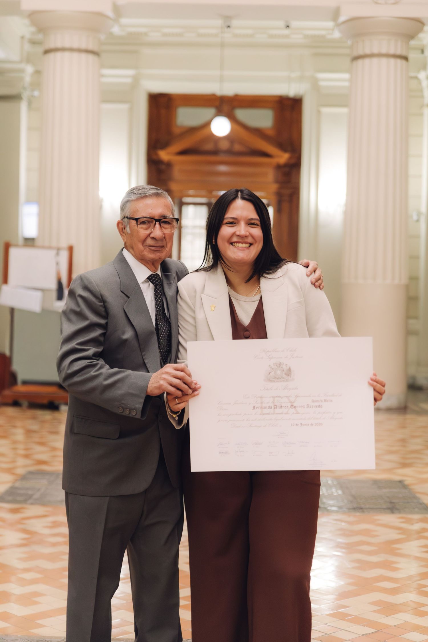 Elderly man and smiling graduate display diploma certificate in elegant hallway.