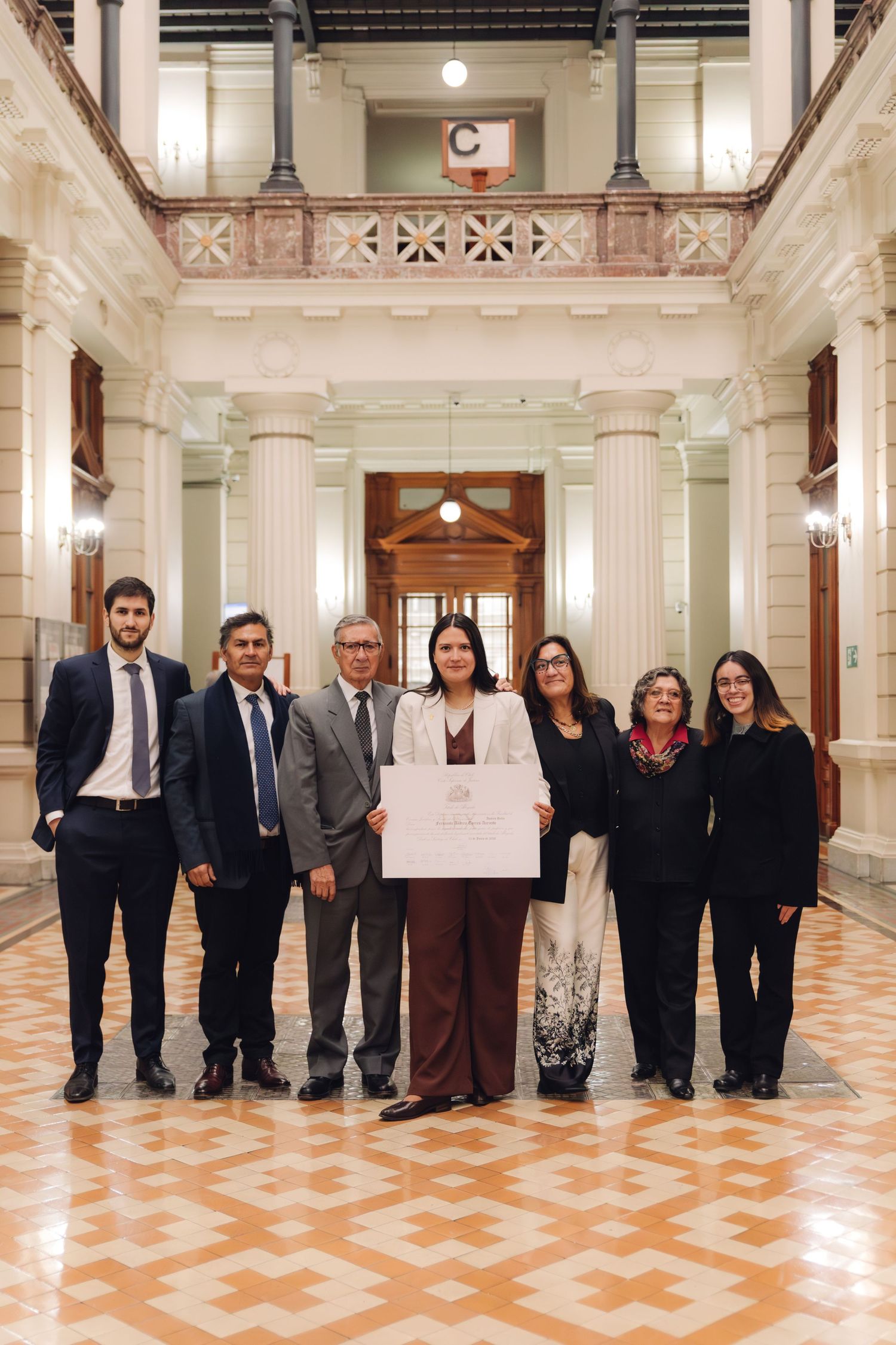 Group of seven professionals pose with certificate in elegant columned building interior.
