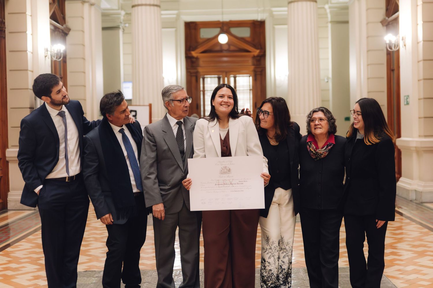 Seven colleagues smile together holding official certificate in ornate classical building.
