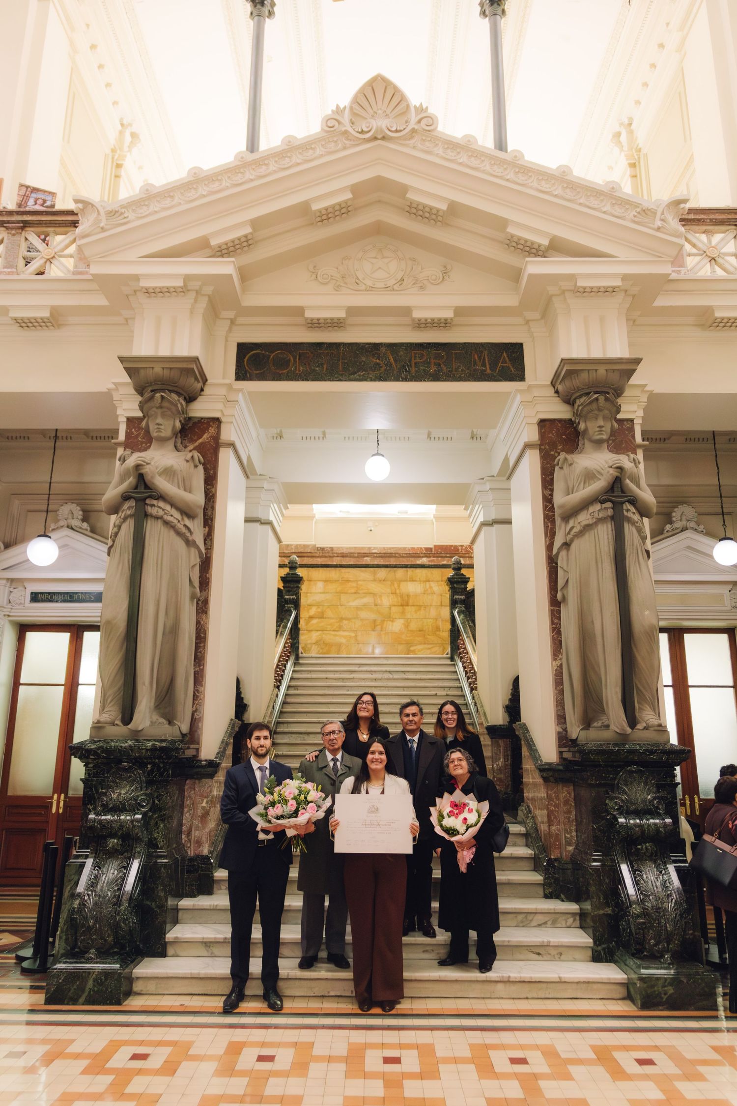 Group poses on steps of Corte Suprema building holding flower bouquets after ceremony.