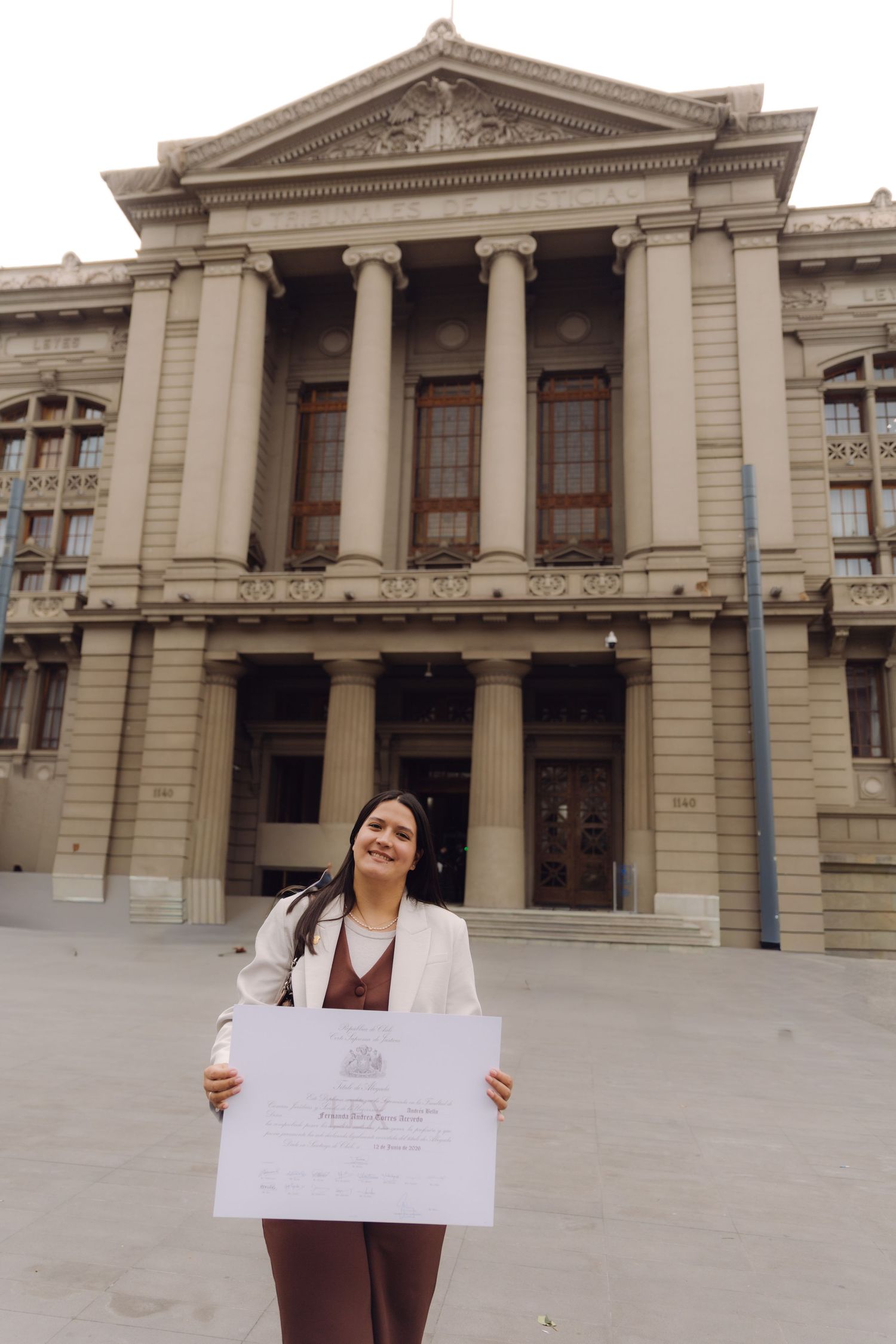 Smiling woman holds official certificate outside grand neoclassical courthouse building.