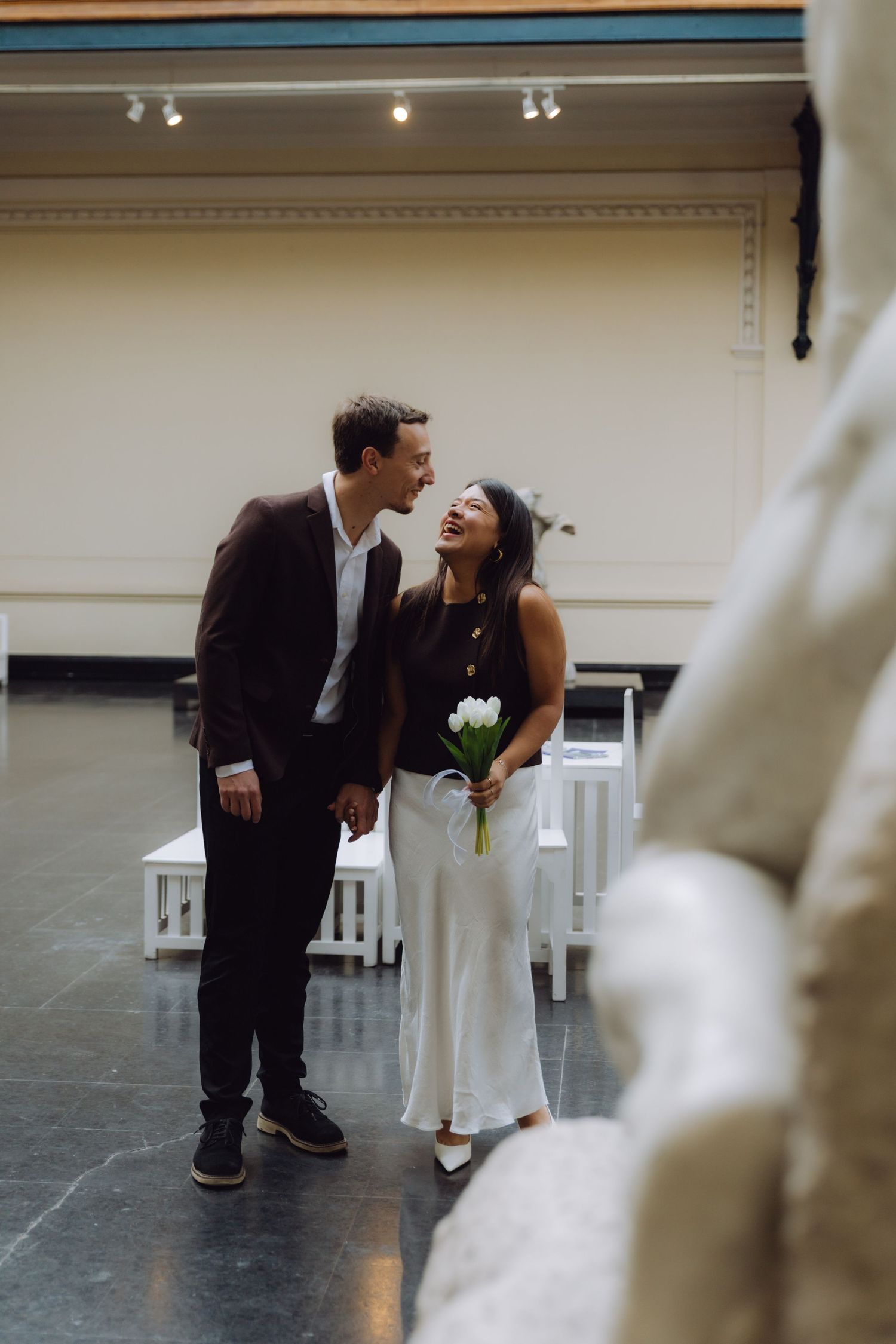 Joyful couple laughing together while walking through a museum gallery with white benches and sculptures.