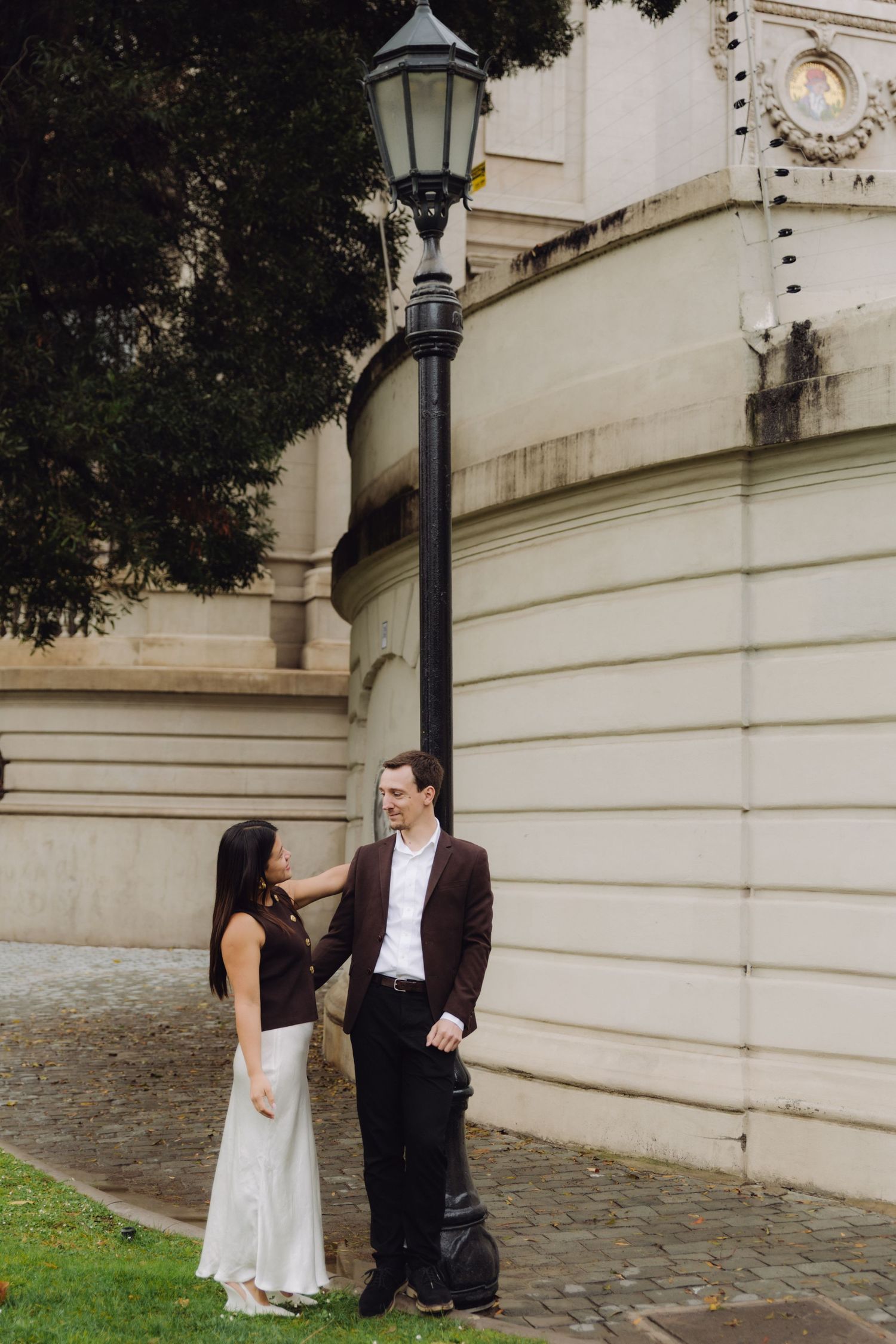 Couple standing together by black street lamp against elegant neoclassical building wall.