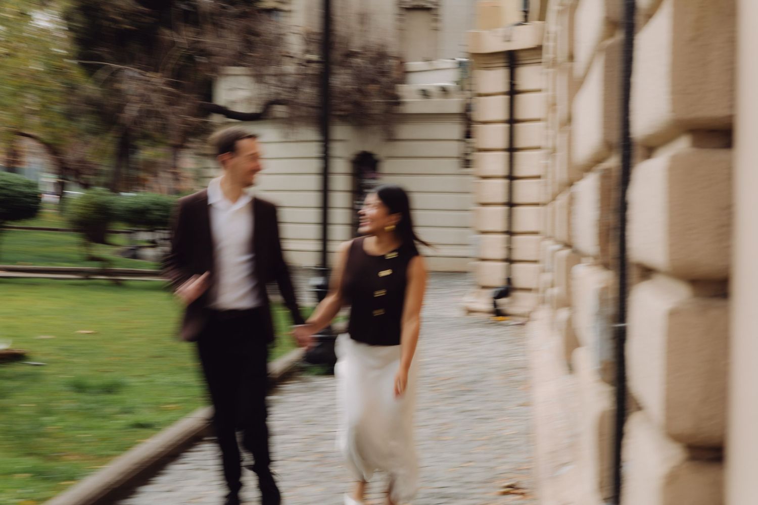 Blurred motion photo of couple holding hands running along cobblestone path together.