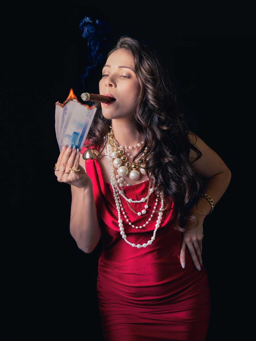 Woman in red dress wearing pearl necklaces, smoking a cigar while burning money against black background.
