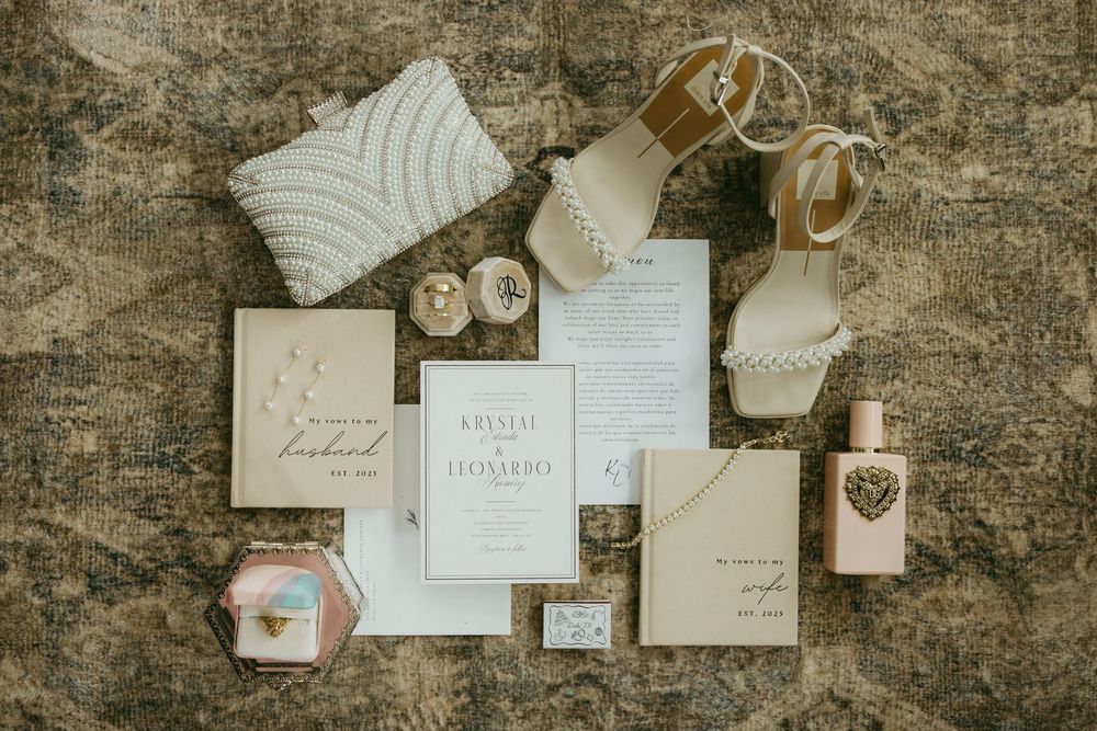Elegant wedding flat lay with invitation suite, perfume, shoes, rings, and accessories on marble.