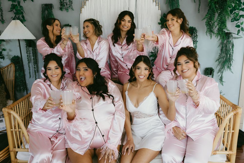 Bridesmaids in pink satin pajamas toasting with champagne glasses during bridal party getting ready.