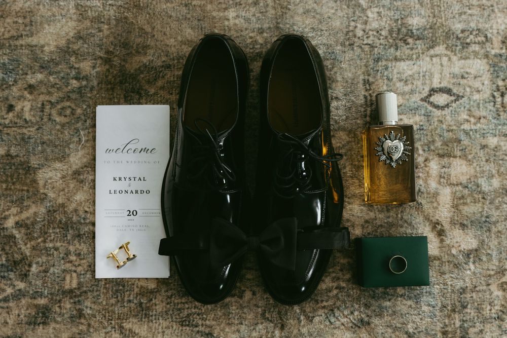 Groom wedding flat lay featuring black patent leather oxford shoes, cologne, ring box, and wedding invitation suite.