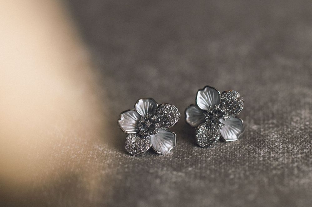 Silver flower stud earrings with crystal details on gray fabric background.