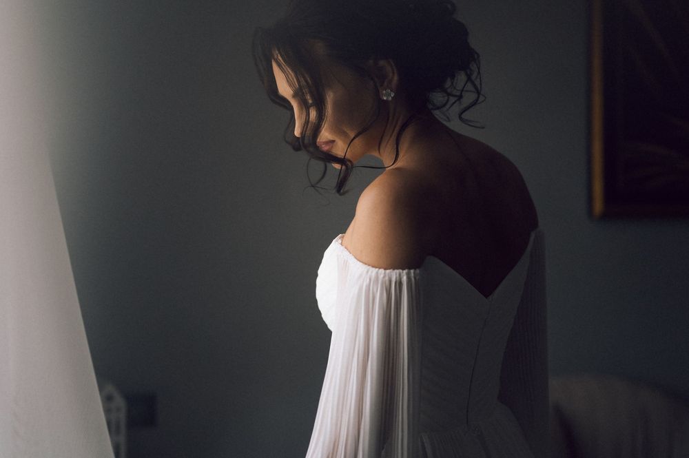 Bride in white strapless wedding gown standing in soft light, looking down gracefully.