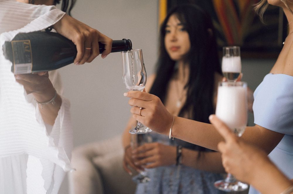 Champagne being poured into a flute glass at a celebration with women in elegant attire.