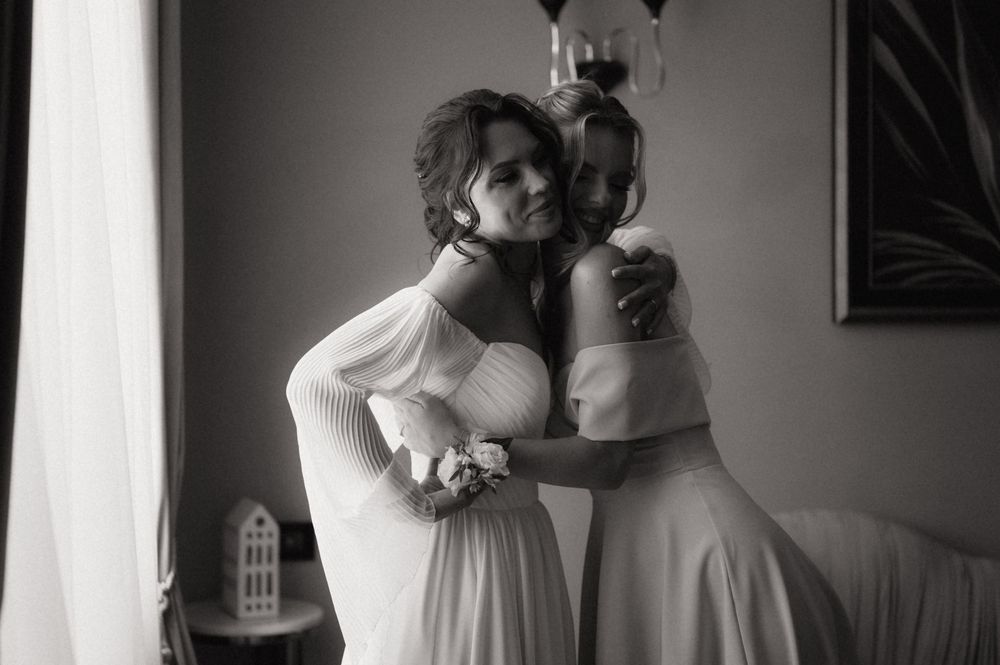 Black and white photo of two women in elegant dresses sharing a tender embrace at a wedding celebration.