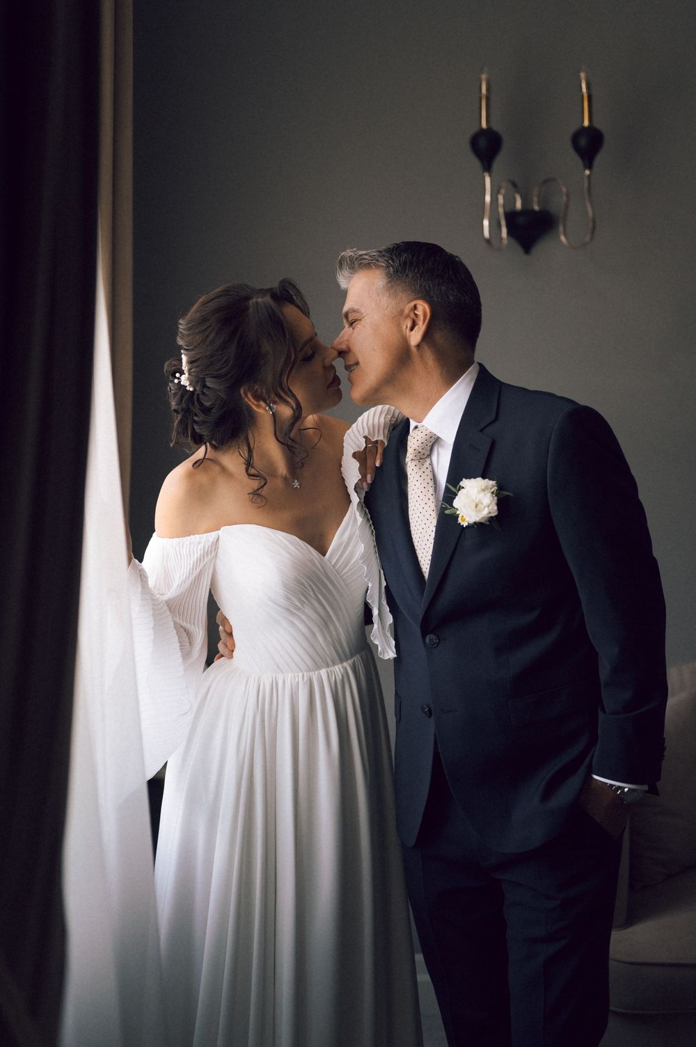 Bride and groom share a romantic kiss in elegant wedding attire, white gown and dark suit with boutonniere.