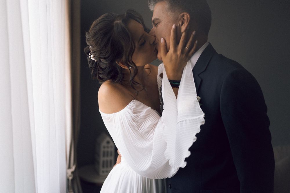 A couple sharing a romantic kiss at their wedding, the bride in an off-shoulder white gown and groom in a dark suit.