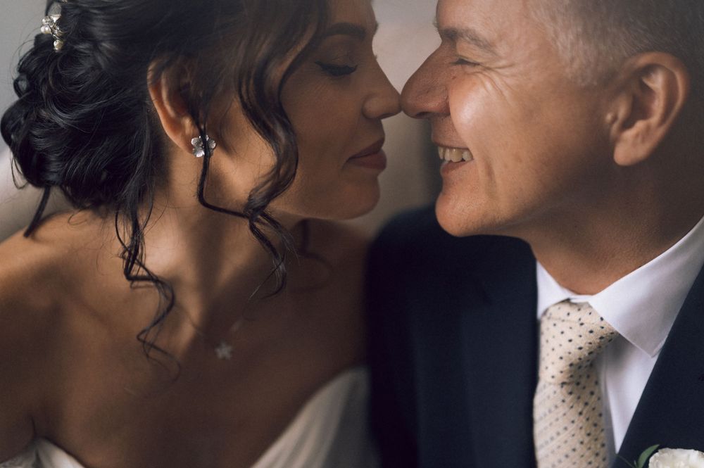 A bride and groom share an intimate moment, nearly kissing, with the groom smiling warmly on their wedding day.