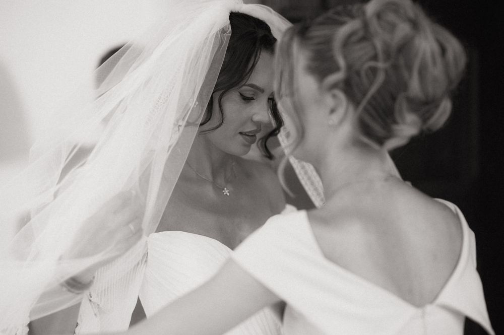 Black and white photo of two brides in white gowns sharing an intimate moment, one wearing a veil.