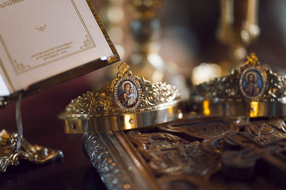 Gold Orthodox wedding crowns with religious icons displayed on a ceremonial tray with candles.