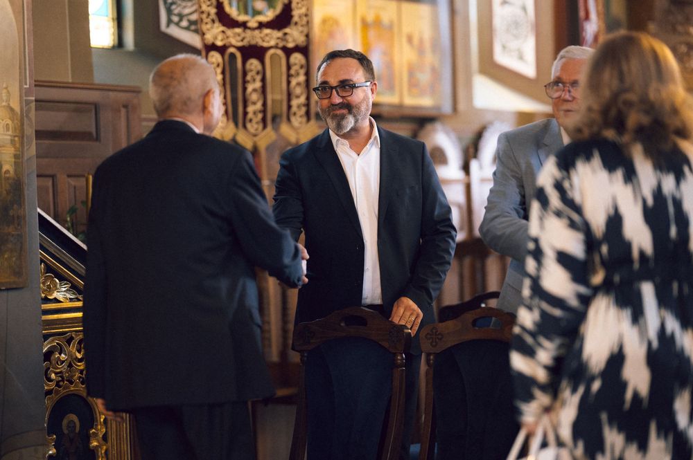 Men in formal attire shaking hands inside an ornate church with golden decor.