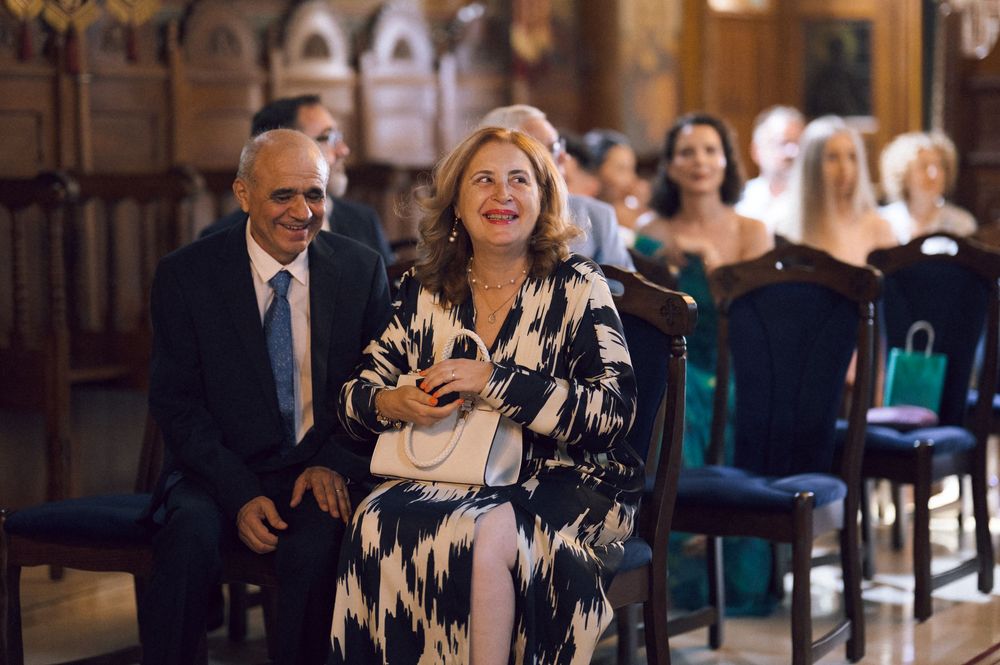 Smiling couple seated at an elegant indoor event, woman in black and white dress, man in suit with tie.