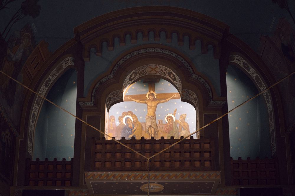 Orthodox church altar with crucifixion fresco, golden iconostasis, and Byzantine religious paintings in dim sacred interior.