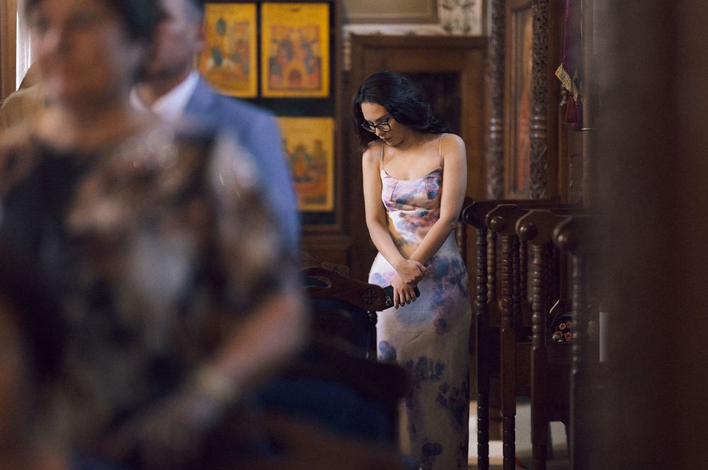Woman in floral dress stands pensively in ornate church interior during a religious ceremony.