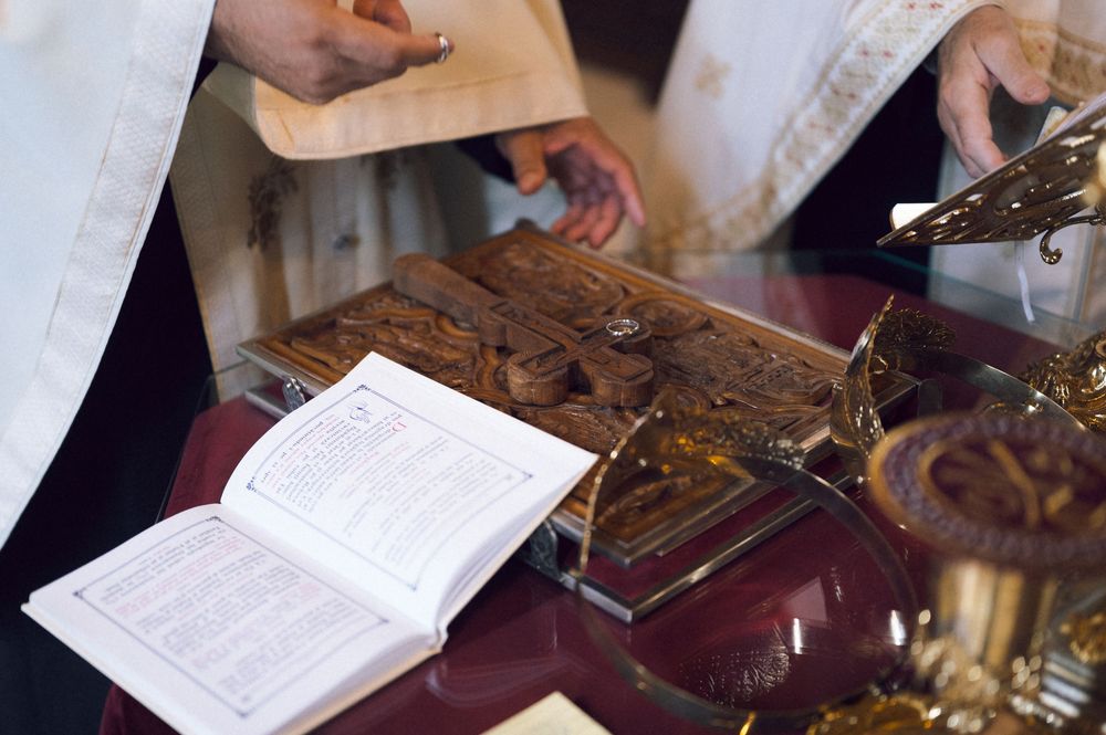 Orthodox Christian priest performing a religious ceremony with a cross, Bible, and golden liturgical items on an altar.