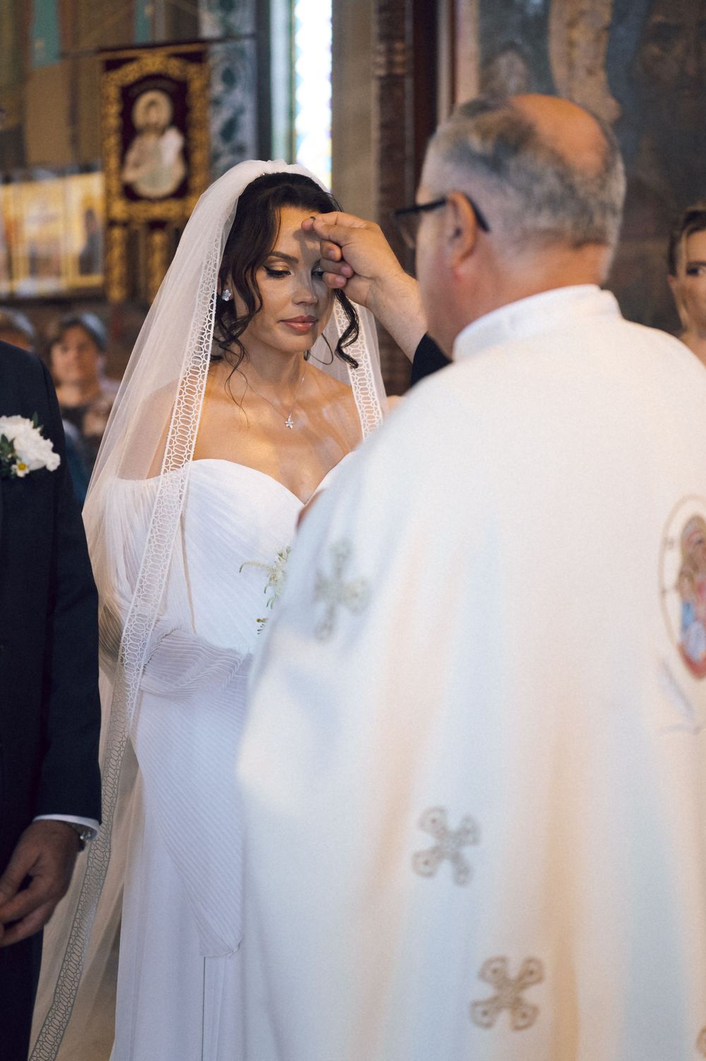 Priest blessing bride in white wedding gown and veil during religious church wedding ceremony.