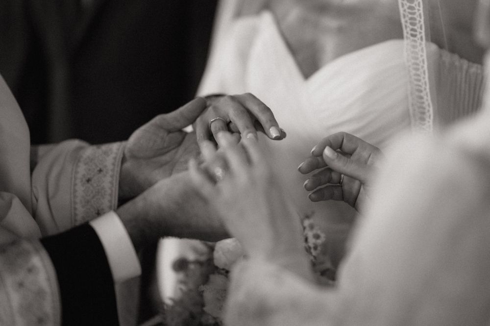 Black and white wedding ring exchange ceremony photo capturing groom placing ring on bride's finger.