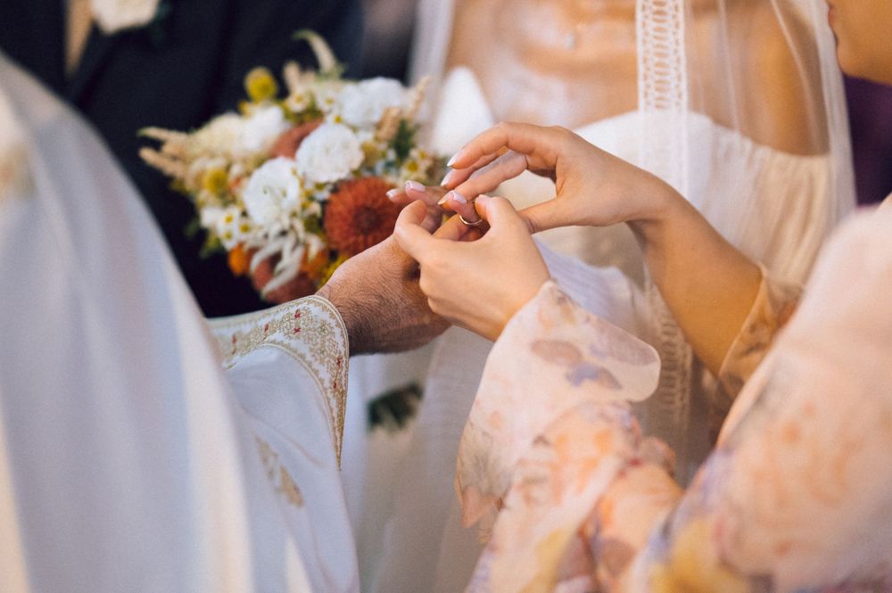 Couple exchanging wedding rings during ceremony, bride holding bouquet of white and orange flowers.