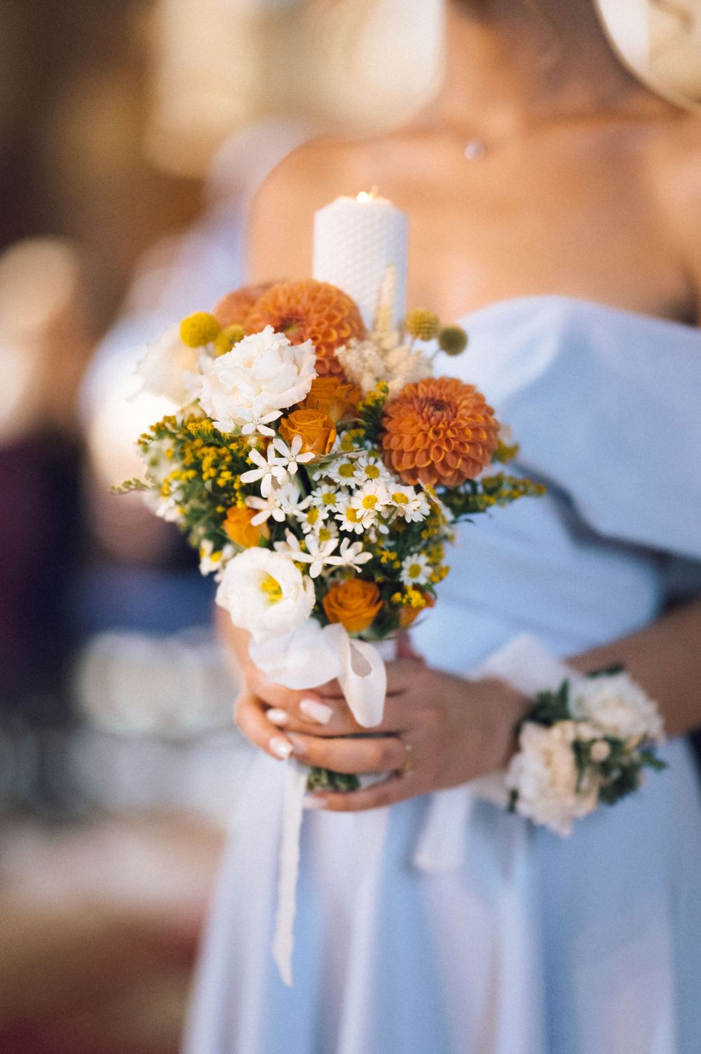 Bridesmaid in light blue off-shoulder dress holding a bouquet of orange dahlias, white flowers, and a white candle.