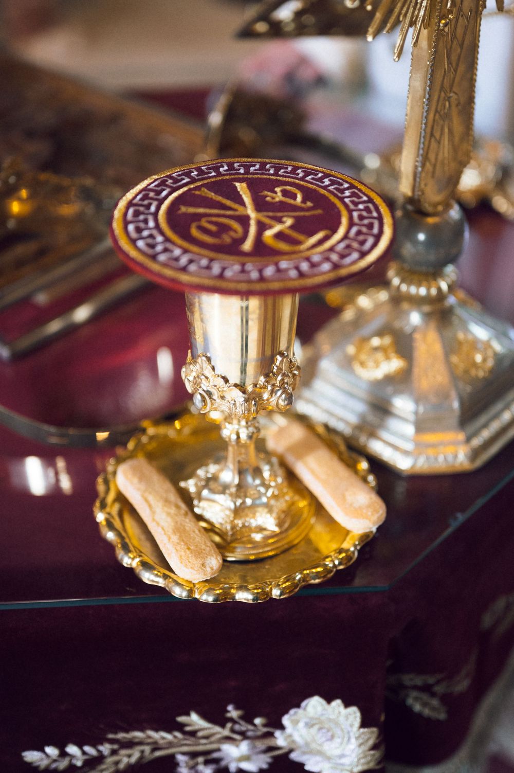 Golden chalice with religious symbols on burgundy altar cloth with sacramental bread during Orthodox Christian ceremony.