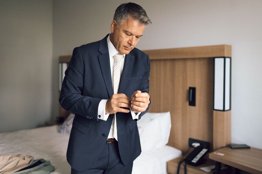 Businessman in navy suit adjusting cufflinks in hotel room before business meeting.