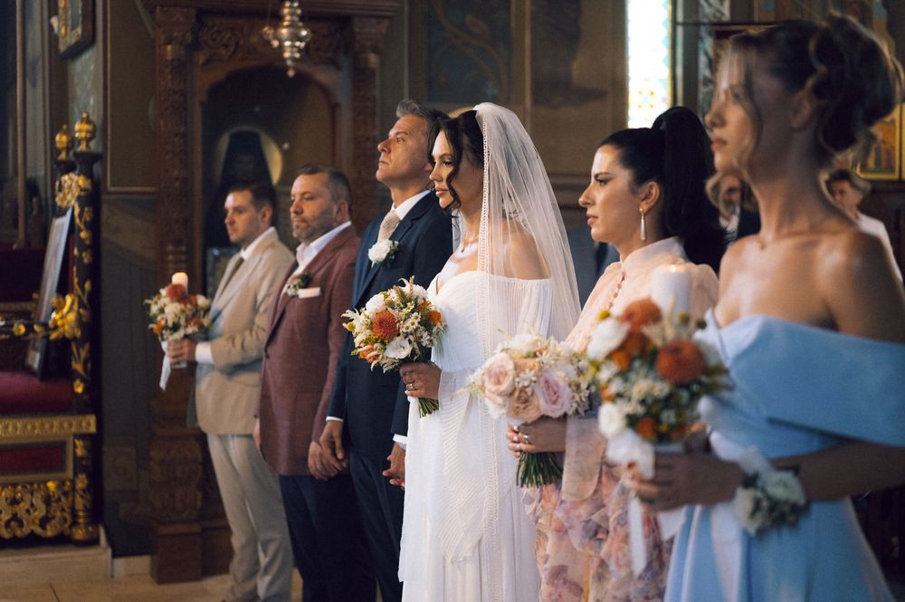 Bride and bridesmaids holding bouquets during a traditional church wedding ceremony with guests standing nearby.