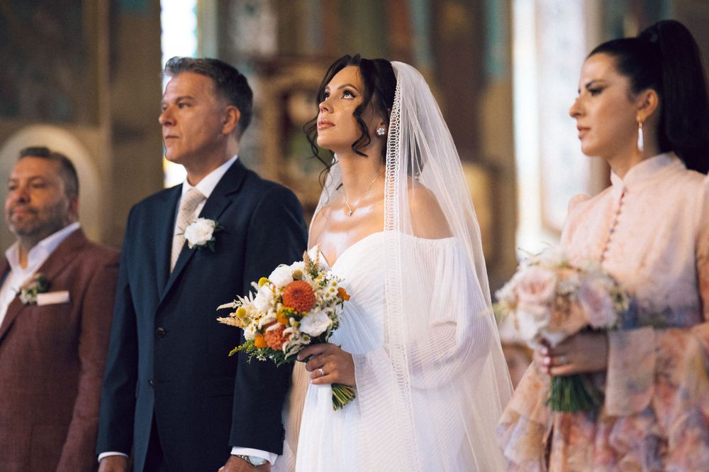 Bride and groom stand at the altar during a wedding ceremony, bride holding a colorful bouquet in a white gown.