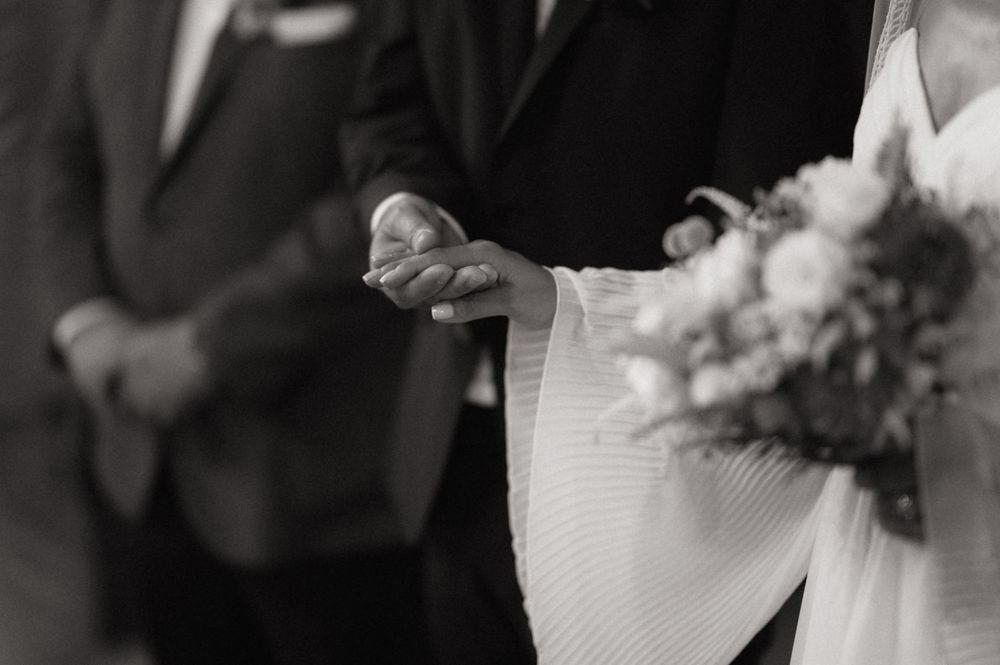 Black and white wedding photo of bride and groom holding hands, bride carrying a bouquet of flowers.
