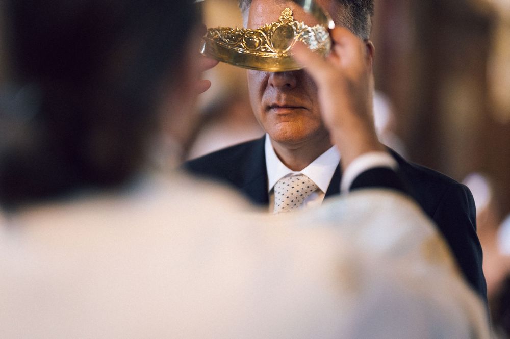Priest holding ornate golden crown over groom during Orthodox wedding ceremony in church.