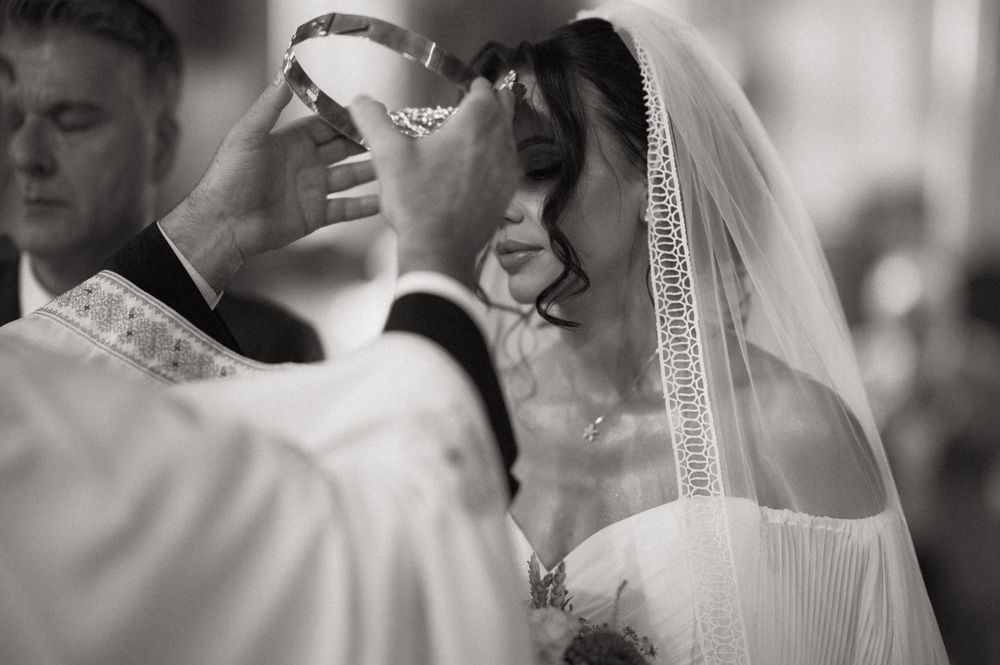 Black and white photo of a bride receiving a crown during a traditional wedding ceremony.