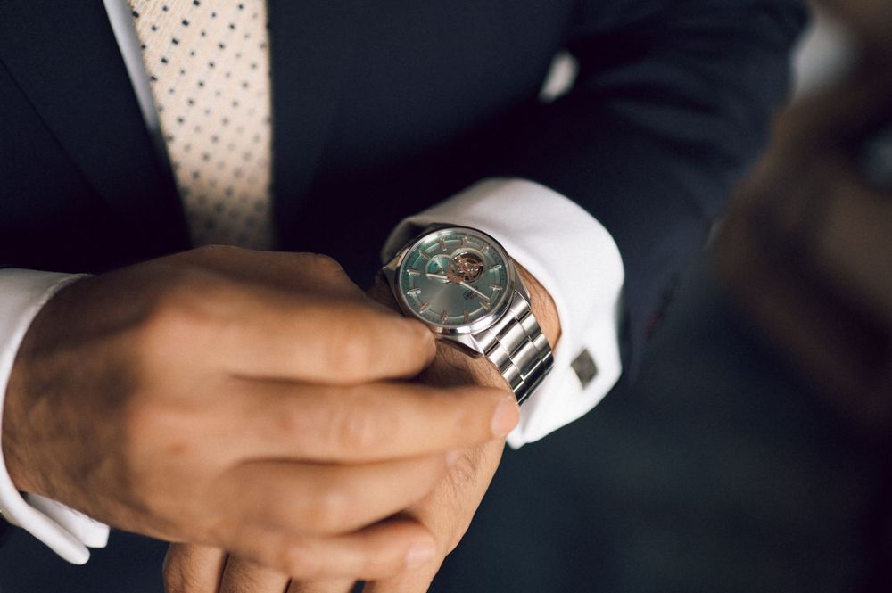 Man in suit adjusting silver luxury wristwatch with cufflinks, close-up of elegant timepiece on wrist.
