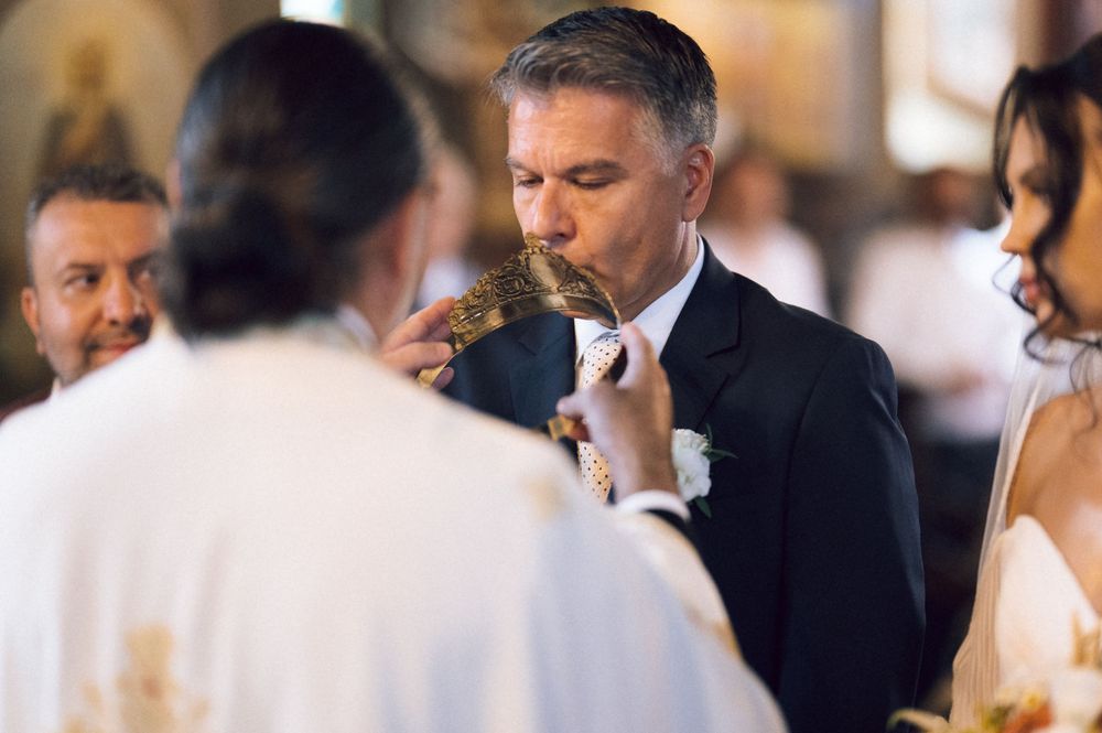 Groom kissing a religious artifact during an Orthodox wedding ceremony with priest in golden vestments.
