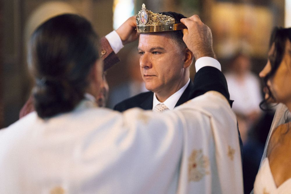 Priest placing a golden crown on a groom during an Orthodox Christian wedding ceremony in a church.