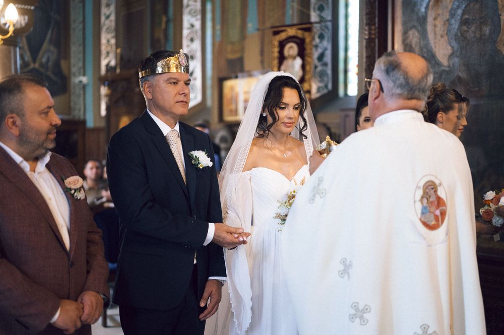 Couple exchanging vows in Orthodox church wedding ceremony with priest and crowned groom in elegant white bridal gown.