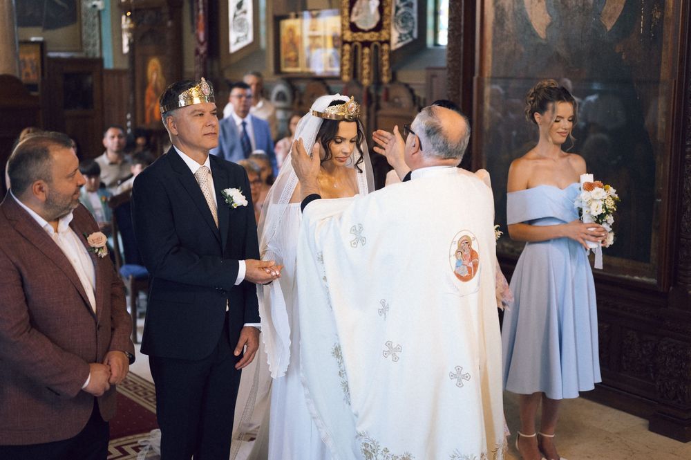 Orthodox wedding ceremony with bride and groom wearing crowns, officiated by a priest in a decorated church.