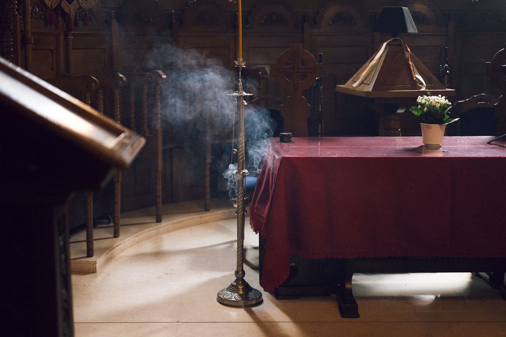 Incense smoke rising from a censer on a stand inside an ornate church with a red altar cloth.