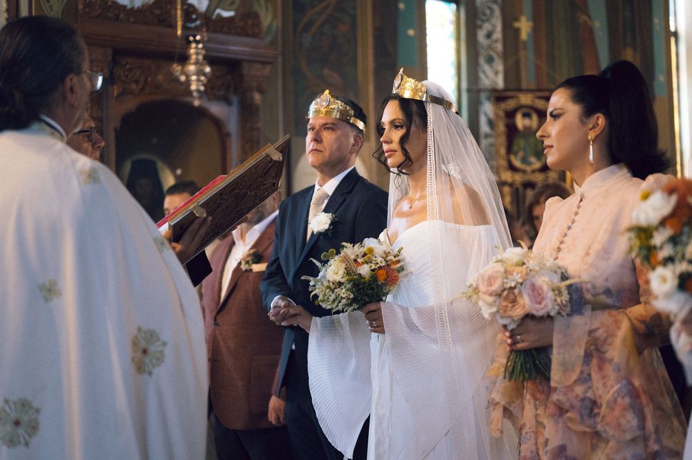 Bride and groom wearing crowns during a traditional Orthodox church wedding ceremony with guests and clergy.